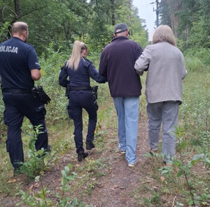 Dwoje policjantów idzie w lesie z mężczyzną i prowadzącą go kobietą.