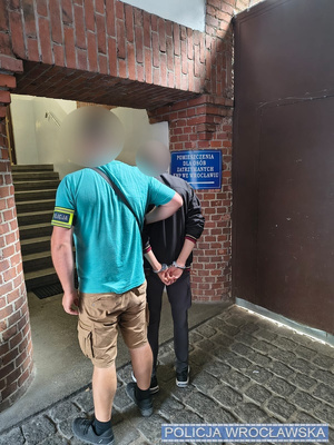 Policjant w cywilu prowadzi zatrzymanego na komendę.
