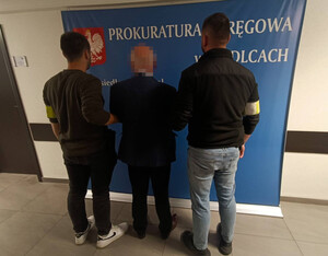 Dwaj policjanci z zatrzymanym mężczyzną zakutym w kajdanki.