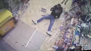 Mężczyzna siedzi na podłodze w zdemolowanym sklepie.