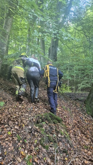 Funkcjonariusze policji i straży pożarnej, odprowadzają kobietę.