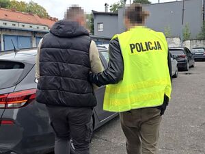 Funkcjonariusz z zatrzymaną osobą w kajdankach.