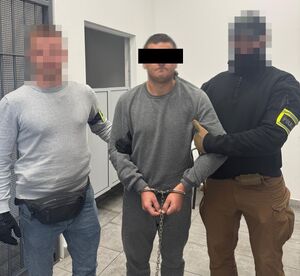 Dwaj policjanci z zatrzymanym, skutym w kajdanki mężczyzną.