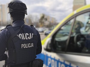 Umundurowany policjant z Grupy Szybkiego Reagowania stoi przy radiowozie - widok z tyłu.