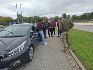 Funkcjonariusz i uczestnicy szkolenia obok samochodu na dworze.