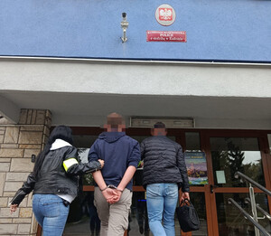 Policjant i policjantka prowadza zatrzymaną osobę.