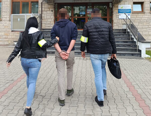 Policjant i policjantka prowadza zatrzymaną osobę.