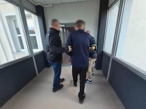 Dwaj policjanci prowadzą korytarzem zatrzymanego mężczyznę.