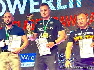 Policjant z innymi zwycięzcami na podium. W rękach trzymają puchary i dyplomy.