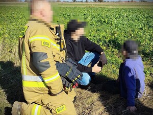 Odnaleziony mężczyzna sieni na ziemi, obok strażak ochotnik i mężczyzna kucają przy nim.