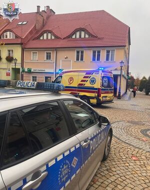 Radiowóz policyjny i karetka pogotowia stoją przy budynku.