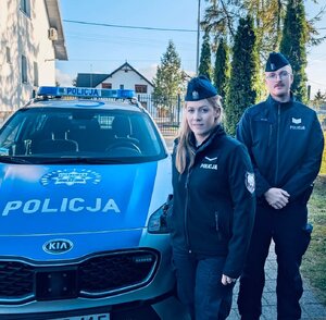Policjant i policjantka stoją przy radiowozie.