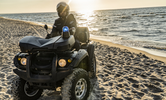 Policjant na quadzie na patrolujący morską plażę w promieniach zachodzącego słońca.