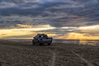 Terenowy oznakowany samochód policyjny na nadmorskiej plaży, w tle zachód słońca i spokojne morze.