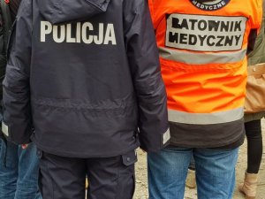 POLICJANT RAZEM Z RATOWNIKIEM, STOJA TYŁEM,WIDAĆ NAPISY