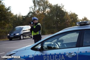 Policjant ruchu drogowego kontroluje prędkość jadących pojazdów - obok policyjny radiowóz.