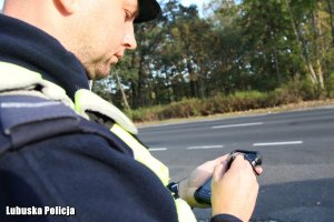 Policjant korzystający z telefonu komórkowego, stojąc przy drodze.