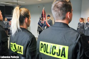 Policjanci stojący w szeregu, w tle sztandar policyjny.