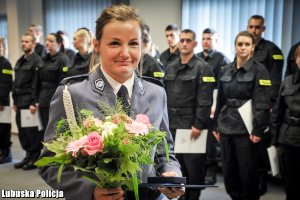 Policjantka z bukietem kwiatów, a w tle policjanci stojący w szeregu.