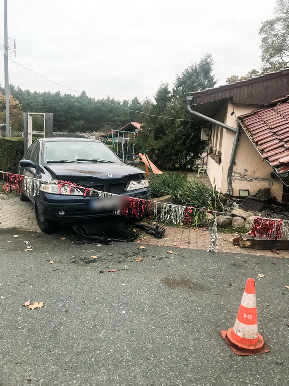 Uszkodzony pojazd osobowy stojący obok budynku.