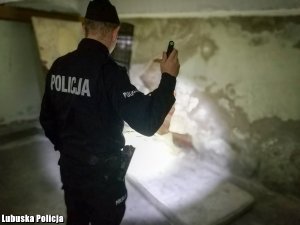 Policjant z włączoną latarką sprawdza czy nie ma osób bezdomnych w opuszczonych pomieszczeniach.