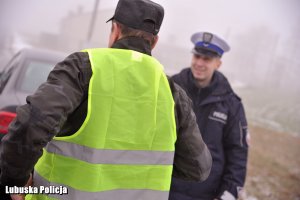 Rowerzysta w kamizelce odblaskowej. W tle policjant