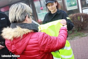 Policjantka wręcza kobiecie kamizelkę odblaskową