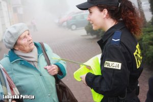 Policjantka wręcza kobiecie kamizelkę odblaskową