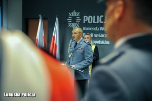 Ramię policjanta, a w tle przemawiający z mównicy policjant.