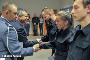 Policjant składa gratulacje policjantom stojącym w szeregu.