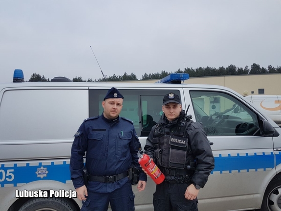 Policjanci z gaśnicą stojący przy radiowozie.