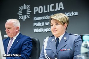 Policjantka, a obok niej inny mężczyzna za stołem prezydialnym.