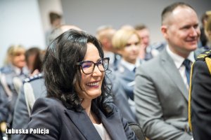 Kobieta siedząca na sali konferencyjnej, a w tle inne osoby.