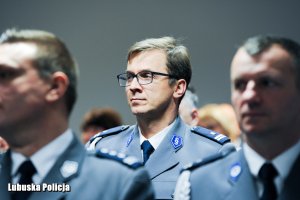 Policjant siedzący na sali konferencyjnej, obok inne osoby.