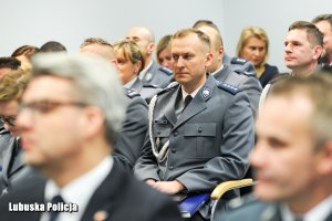 Policjant siedzący wśród innych policjantów na sali konferencyjnej.