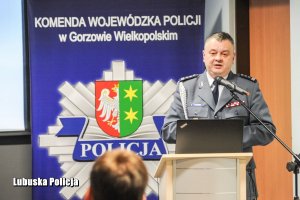 Policjant przemawiający z mównicy do mikrofonu.