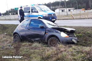 Policyjny radiowóz i policjant. W rowie rozbite auto