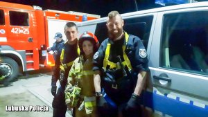 Policjanci i funkcjonariuszka straży pożarnej przed radiowozem