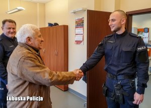 Policjant podaje rękę starszemu mężczyźnie w pomieszczeniu w komendzie.