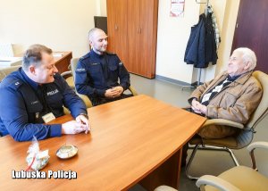 Policjanci i mężczyzna siedzą przy stole w pomieszczeniu.