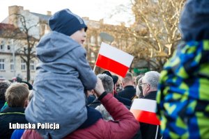 Dziecko podniesione przez ojca z flagą Polski, a w tle inne osoby.