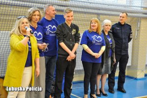 Osoby stojące przy siatce ochronnej na sali gimnastycznej. Kobieta przemawia do mikrofonu.
