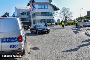 Policyjny radiowóz, a obok niego samochód osobowy - w tle budynek uniwersytecki.