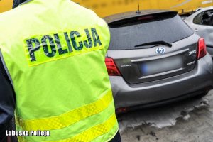 Policjant w kamizelce odblaskowej na tle odzyskanego auta toyota yaris