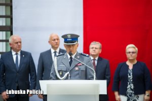 Inspektor Policji przemawia. W tle flaga biało- czerwona