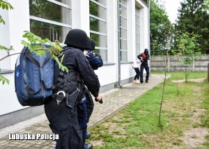 Policjanci przygotowani do szturmu zbliżają się do napastnika trzymającego zakładniczkę