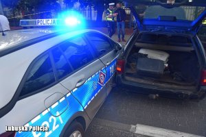 Policyjny radiowóz przy uszkodzonym pojeździe - w tle policjant i mężczyzna.