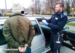 Policjant z zatrzymanym mężczyzną przy radiowozie.