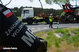 Emblemat żandarmerii wojskowej i w tle policjant z miernikiem prędkości