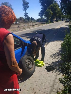 Kobieta przypatrująca się jak policjant wymienia jej koło